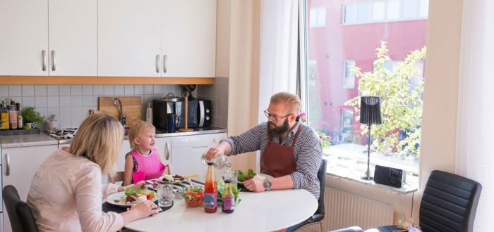 Vuxna och barn sitter runt ett matbord och äter tillsammans i köket.